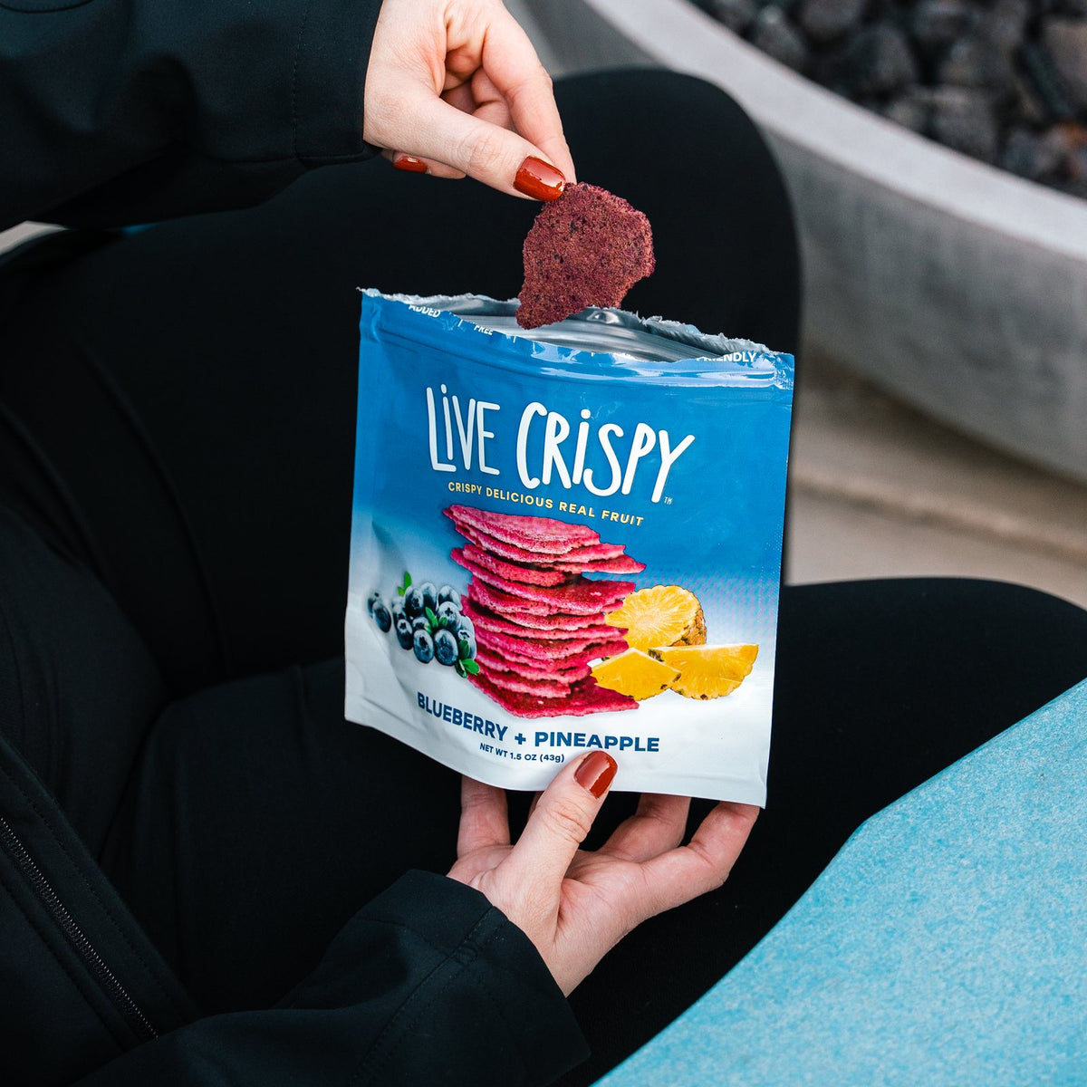 Open bag of Blueberry and Pineapple fruit chips with a chip in hand