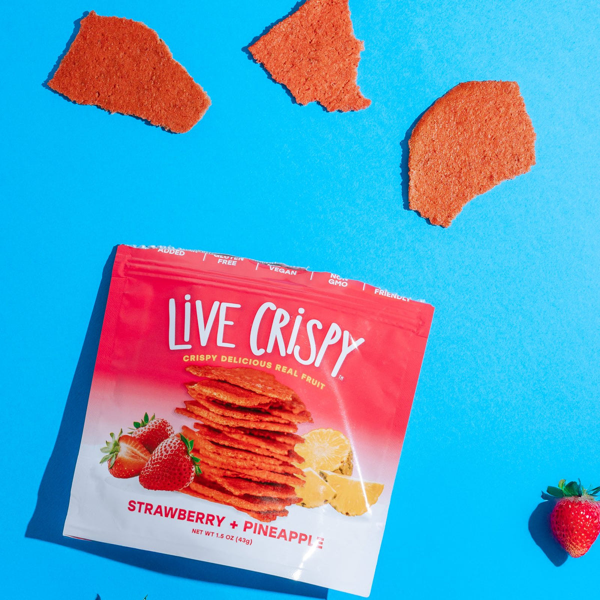 Strawberry and Pineapple bag with three baked fruit chips and fresh strawberries on a blue background