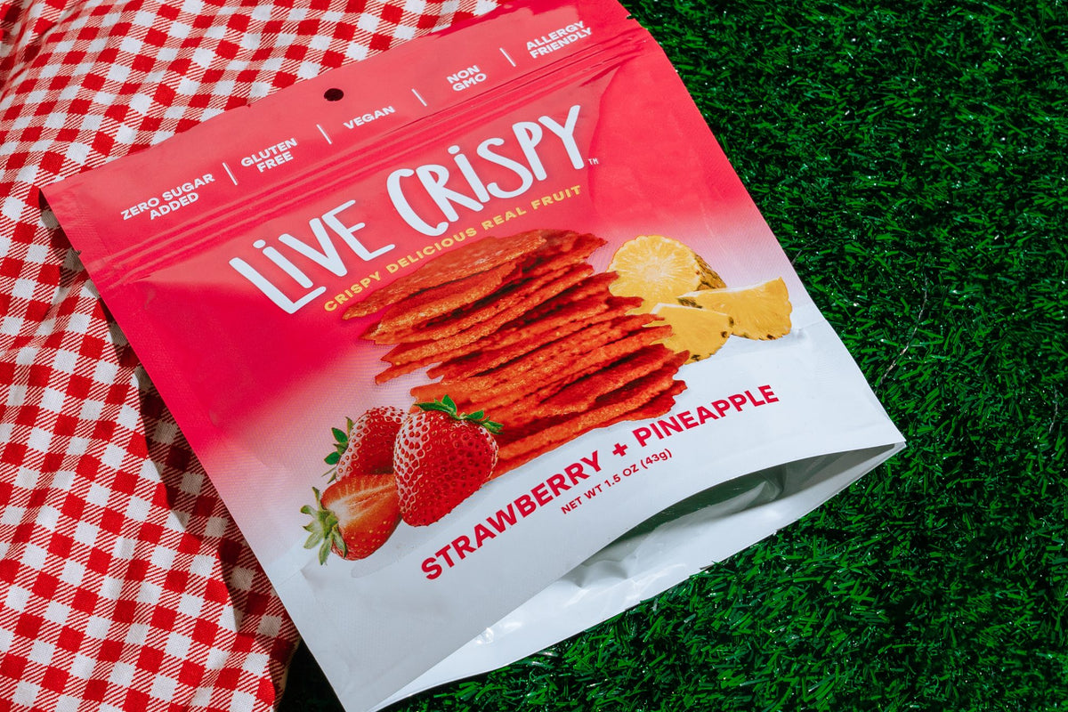 A bag of Live Crispy Strawberry and Pineapple on a gingham picnic blanket